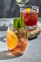 Orange Gin tonic cocktail for lifestyle design. Summer cocktail concept background. Gin tonic drink with orange slice and banana leaf. Cocktail glass on vintage table with sunshine and harsh shadow.