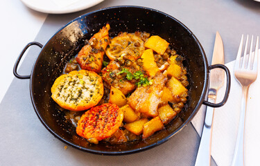 Delicious roasted monkfish with lemon, potato and green peas served in iron pan with toasted bread