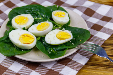 Boiled eggs with fresh spinach leaves and sesame seeds on wooden table