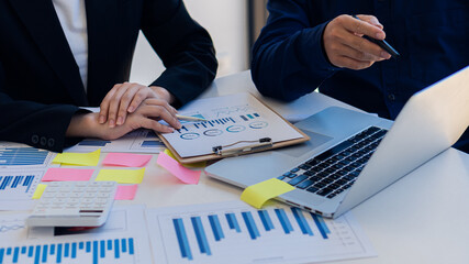 Businessmen discuss charts and analyze graphs showing successful teamwork on a desk with laptop and calculator.