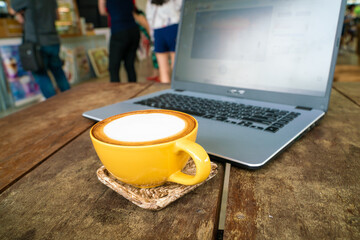 Hot latte art coffee with laptop on wooden table