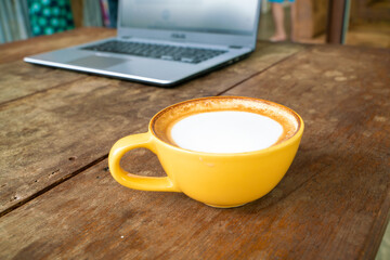 Hot latte art coffee with laptop on wooden table
