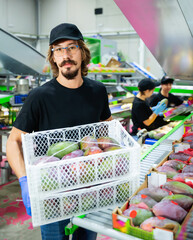 Focused diligent positive male worker working at fruit warehouse carrying box with mangos