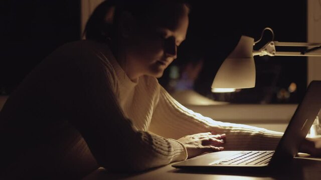 Tired woman. Hard working. Freelance job. Project deadline. Exhausted lady going to sleep on workplace with laptop table lamp light evening home interior dark window.