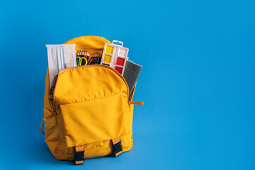 Yellow backpack with school supplies on blue background