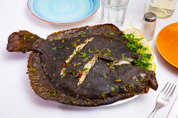 Whole baked brill fish served with sliced lemon and chopped greens..