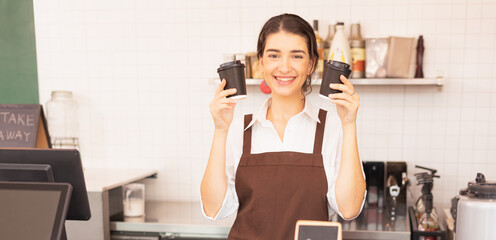 Beautiful caucasian barista woman happy to hold two takeaway hot coffee cups at the coffee bar in cafe coffee shop
