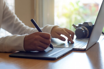 Young female graphic designer using digital tablet with electronic pen and work on laptop computer ...