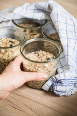Frau mit Brotteig von Vollkorn Brot mit Kürbiskernen, Haferflocken, Sonnenblumenkernen, Chia und Leinsaat roh im Glas für Einkochen und Vorrat auf Tuch und Holz Hintergrund hell