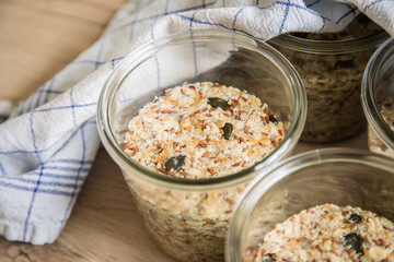 Brotteig von Vollkorn Brot mit Kürbiskernen, Haferflocken, Sonnenblumenkernen, Chia und Leinsaat roh im Glas für Einkochen, Vorrat und Speisekammer auf Tuch und Holz Hintergrund hell