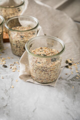 Brotteig von Vollkorn Brot mit Kürbiskernen, Haferflocken, Sonnenblumenkernen, Chia und Leinsaat roh im Glas für Einkochen und Vorrat auf Leinentuch, Holzbrett und Marmor Hintergrund hell