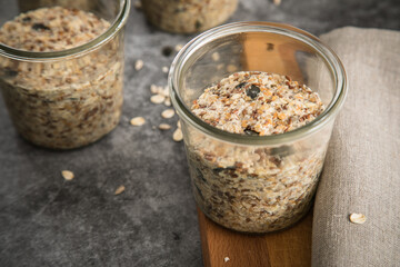 Brotteig von Vollkorn Brot mit Kürbiskernen, Haferflocken, Sonnenblumenkernen, Chia und Leinsaat roh im Glas für Einkochen und Vorrat auf Leinentuch, Holzbrett und Marmor Hintergrund dunkel