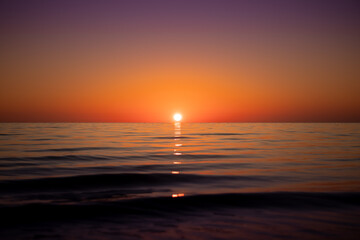 Distant Sun setting in clear skies over a calm and serene ocean of perfection