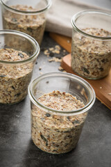 Brotteig von Vollkorn Brot mit Kürbiskernen, Haferflocken, Sonnenblumenkernen, Chia und Leinsaat roh im Glas für Einkochen und Vorrat auf Leinentuch, Holzbrett und Marmor Hintergrund dunkel