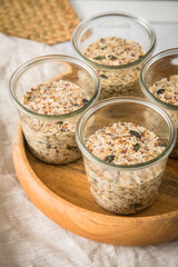 Brotteig von Vollkorn Brot mit Kürbiskernen, Haferflocken, Sonnenblumenkernen, Chia und Leinsaat roh im Glas für Einkochen und Vorrat auf Leinentuch, Holzbrett und Marmor Hintergrund hell