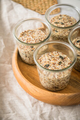 Brotteig von Vollkorn Brot mit Kürbiskernen, Haferflocken, Sonnenblumenkernen, Chia und Leinsaat roh im Glas für Einkochen und Vorrat auf Leinentuch, Holzbrett und Marmor Hintergrund hell
