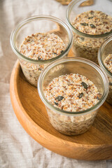Brotteig von Vollkorn Brot mit Kürbiskernen, Haferflocken, Sonnenblumenkernen, Chia und Leinsaat roh im Glas für Einkochen und Vorrat auf Leinentuch, Holzbrett und Marmor Hintergrund hell
