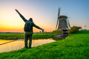Male tourist near traditional windmill at sunset in Netherlands