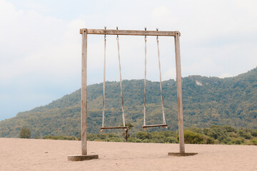 The old rope wooden swing on the desert or sandy beach with mountain background