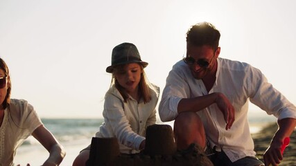 Dad together with son building sandcastle on beach. Planting green flag on top of highest tower. Against afternoon sun. Summer at seaside.