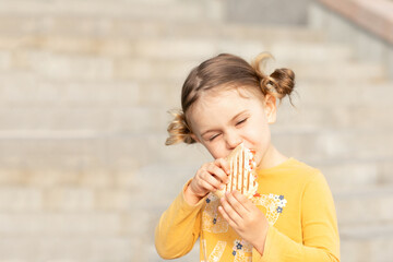 Child girl bites sandwich in the street. Kid eating plain slice of bread outside and enjoy meal