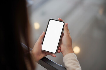 Backside view of woman hand using mockup white screen mobile phone.