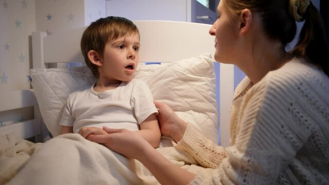 Little sick boy coughing in bed and talking to his loving mother. Concept of child virus and kids protection during coronavirus Covid-19 pandemic.