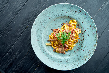 Traditional pasta spaghetti with cream sause, beef and tomato, arugula, served in a blue plate on a black, wooden background. Italian cuisine