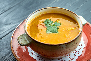 Traditional Moroccan soup - Harira, yellow lentil soup with cilantro in a red plate on a black wood background. Diet soup