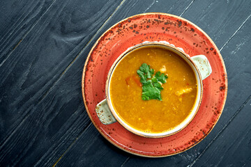 Traditional Moroccan soup - Harira, yellow lentil soup with cilantro in a red plate on a black wood background. Diet soup
