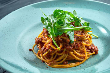 Traditional pasta spaghetti with minced meat and tomato bolognese sauce with arugula, served in a blue plate on a black, wooden background. Italian cuisine