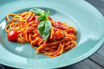 Traditional pasta spaghetti Arrabbiata sauce (with red garlic, paprika and tomato) with basil, served in a blue plate on a black, wooden background