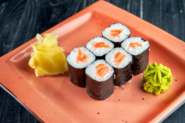 Appetizing Japanese sushi - maki with salmon served in a plate with ginger and wasabi on a black wood background. Japanese cuisine