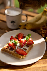 Closeup view of breakfast belgium waffles with strawberry and banana with mint on wooden background. High quality photo