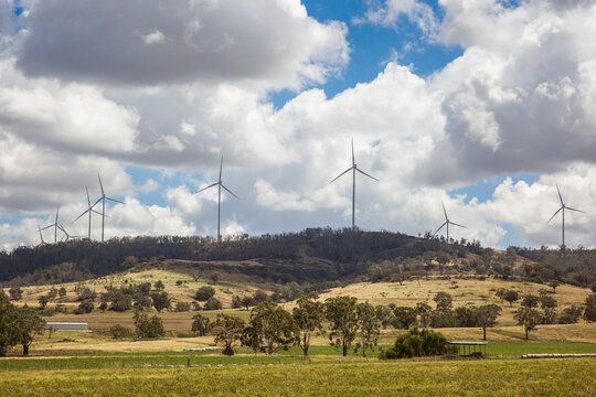 Wind turbines on top of hill above paddocks on farm with cloudy sky