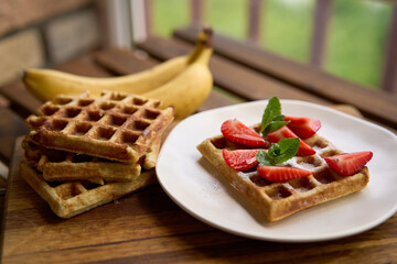 Closeup view of breakfast belgium waffles with strawberry and banana with mint on wooden background. High quality photo