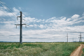 Fototapeta na wymiar High voltage power lines, landscape on a green field at noon, bright sunny day, blue sky with clouds. Energy supply for urban life