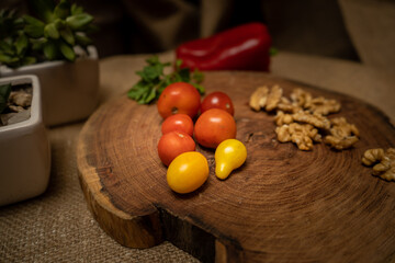 Close-up of cherry tomatoes on a wooden board with various vegetables and ingredients behind.