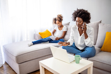 Mother working on laptop at home, while her child using tablet. Girl and mother using tablet and laptop. Modern family. Busy Mother Working From Home With daughter