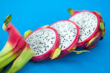 Slices of dragon fruit or pitaya with pink skin and white pulp with black seeds on blue background....