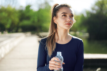 Portrait of young beautiful woman wearing blue sportswear drinking water at park