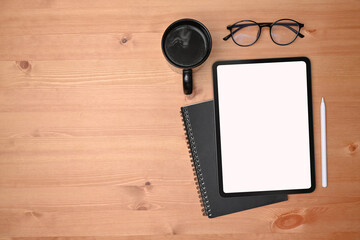 Overhead shot of digital tablet, coffee cup and glasses on wooden desk.