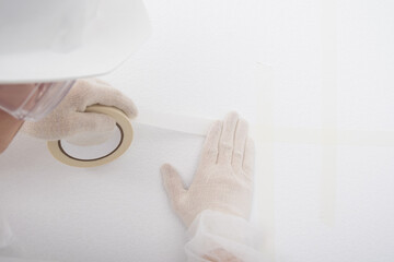 a worker glues an adhesive tape to the joint between a wall and a ceiling, close-up