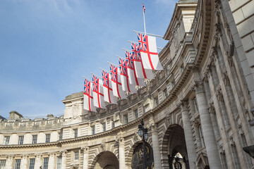 British flags floating on Admiralty Arch near Trafalgar square on a cloudy blue sky, London, United Kingdom