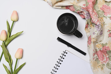 Empty notebook, coffee cup, pen and pink tulips on white background.