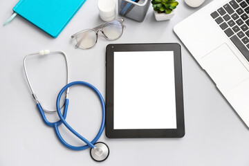 Tablet computer with stethoscope and laptop on grey background