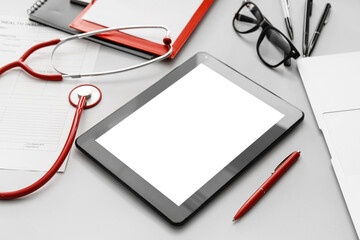Tablet computer with stethoscope and accessories of doctor on grey background