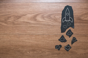 A piece of paper with rocket icon and smoke on wooden background with copy space.
