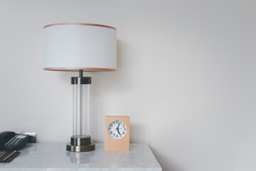 A wooden framed alarm clock sits on the left-hand side, resting on a marble table and bedside lamp.