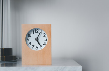 A wooden framed alarm clock sits on the left-hand side on a marble table.